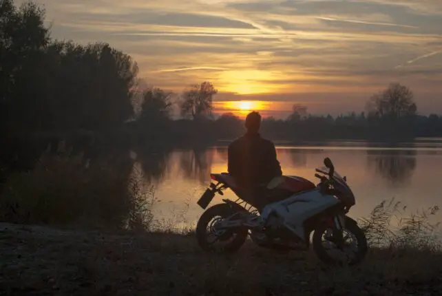 man riding motorcycle on river during sunset